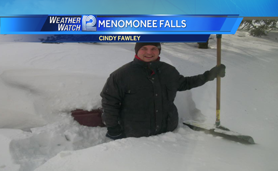 News reporter standing with shovel in 3-4 feet of snow in Menomonee Falls 