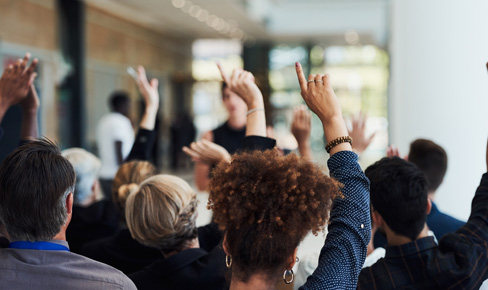 Crowded room with hands raised, camera shows the back of participants heads.