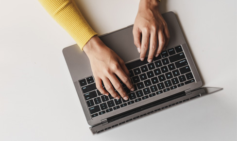 Photo from high angle showing laptop on table, with hands typing on keyboard.