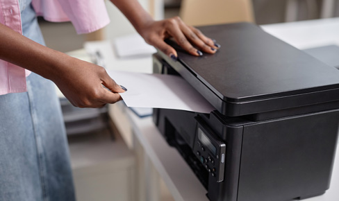 Office printer with person reaching to grab paper that is being printed.